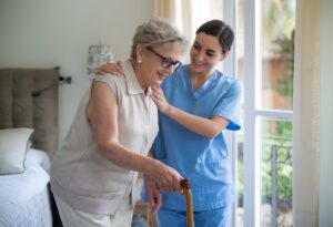 Female caregiver Helping the elderly women to stand up from the bed with using walking stick in the home